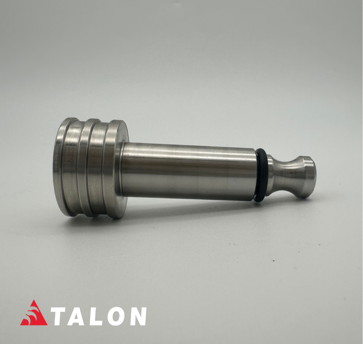 A metallic silver cylindrical mechanical component with a threaded flange on one end and a tapered tip on the other, shown on a light gray background. A red and white TALON logo is visible in the bottom-left corner.