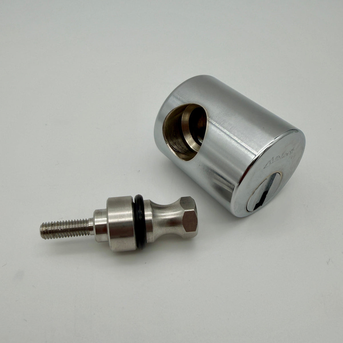 A polished chrome cylinder lock body shown alongside a matching threaded lock pin with a black rubber O-ring, set against a plain light gray background.